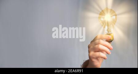 Hand holding glowing light bulb,finding innovative solutions and creative ideas, being unique, thinking different concept isolated on gray background Stock Photo