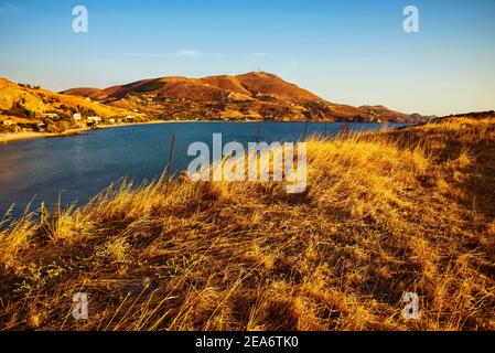 Sea, golden grass on meadow and hills near village Kaspakas in sunset, island Lemnos, Greece. Stock Photo