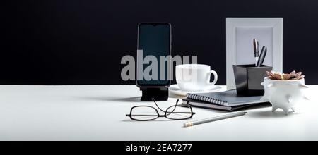 Home Office workspace. Desktop with smart phone template blank, notepads pens office suppliers cup of coffee drink plant. White work desk table on Stock Photo