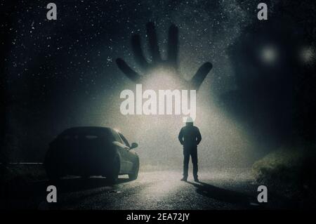 An encounter with a huge alien appearing out of the sky. With a lone man standing next to a car on a spooky night Stock Photo