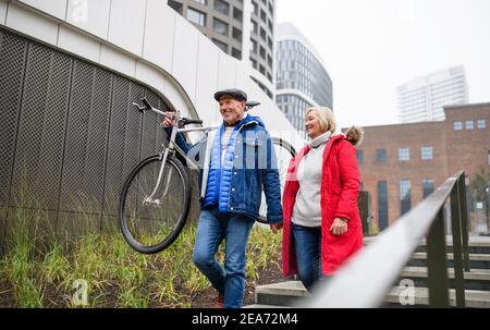 Happy senior couple with bicycle walking in city, holding hands. Stock Photo