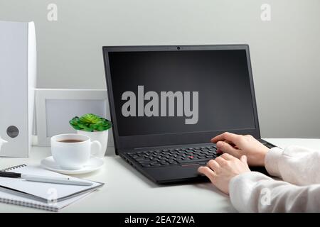 Woman works on laptop in online education on workspace. Female hands typing on laptop. Black laptop display Mock up blank. Workplace in home office Stock Photo