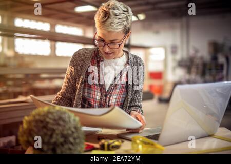 Young focused woman engineer looking at some projects in her workshop. Stock Photo