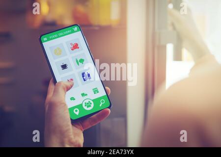 woman looks inside the fridge and using smart phone app to order food delivery Stock Photo