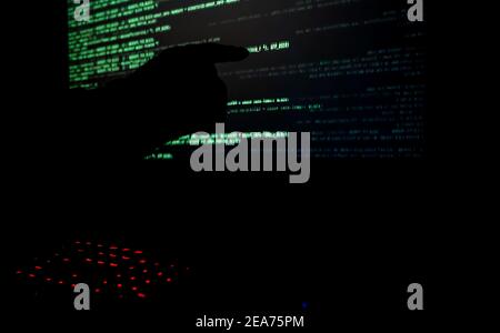Hacker pointing to code on a computer monitor in a dark room.  Stock Photo