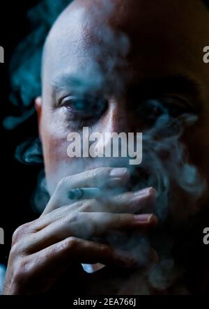 Man smoking a cigarette blowing out white smoke.  Stock Photo