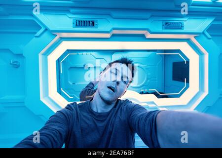 Happy caucasian client of a futuristic capsule hotel takes a selfie near the mirror before going to sleep. The modern interior references to a cryogen Stock Photo