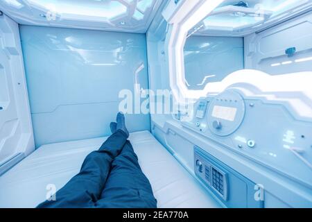 A man rests and sleeps in a capsule hotel view from the inside. The interior resembles a cryocapsule in a spaceship Stock Photo