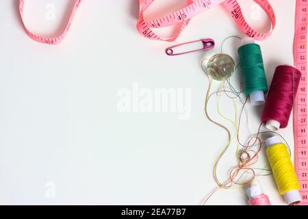Reels of multicolored thread, pink measuring tape, and a pink pin on a white table flatlay. Needlework, sewing, and repair of the clothes. Space for t Stock Photo