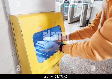 Passenger disinfects and washes hands in a special device with a sanitizer at the public transport station. Stock Photo