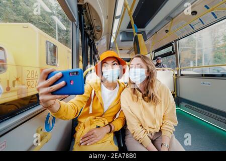 02 September 2020, Moscow, Russia: Two friends taking selfie photos in medical masks in the Moscow bus. Coronavirus restrictions and quarantine on pub Stock Photo