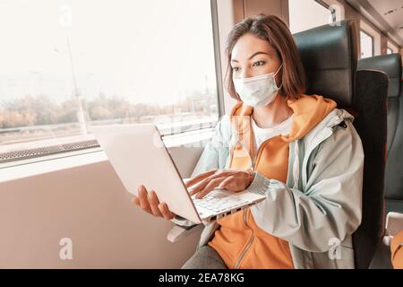 Young Asian woman wears a medical mask and works or studies on her laptop. Travels in a modern train Stock Photo