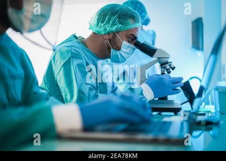 Medical workers in hazmat suit working with microscope and laptop computer inside modern laboratory hospital - Focus on center face Stock Photo