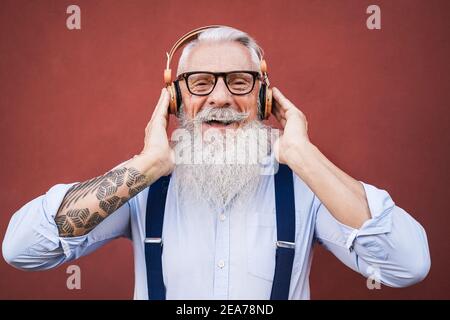 Happy hipster senior man listening to playlist music outdoors - Focus on face Stock Photo