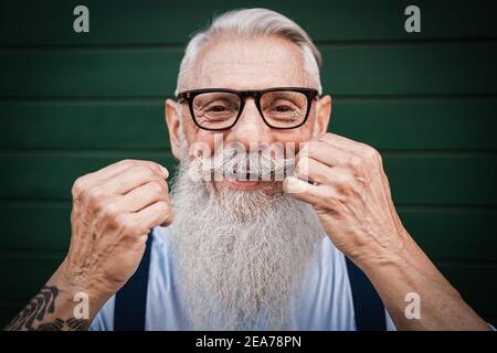 Portrait of happy hipster senior man with green background - Focus on mustache