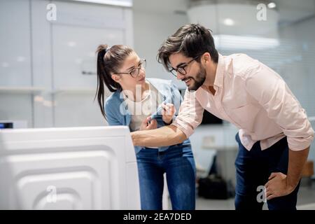 Young couple choosing washing machine while standing in whiteware department. Stock Photo