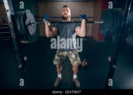 Muscular caucasian bearded man lifting weights in gym. Stock Photo