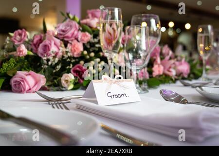 Groom wedding breakfast place setting with name card on top table waiting for arrival with bride and pink roses and shiny champagne glasses Stock Photo