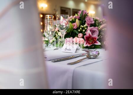 Groom wedding breakfast place setting with name card on top table waiting for arrival with bride and pink roses and shiny champagne glasses Stock Photo