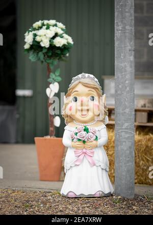 Wedding day large bride garden gnome holding bouquet at wedding with flowers and barn in background Stock Photo