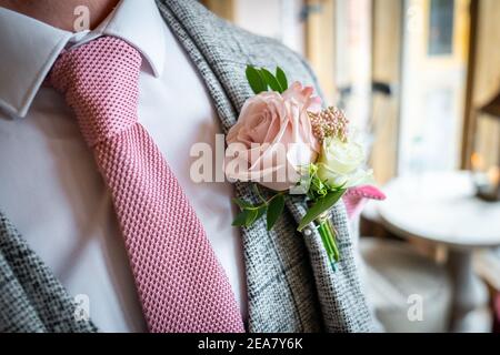 Close up of pink rose wedding boutonniere with green leaves and stalk on grooms suit jacket with matching tie colour looking smart on day of ceremony Stock Photo