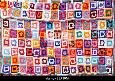 Colorfull handmade crochet blanket afgan made from woolen granny squares hanging outdoors on the string Stock Photo