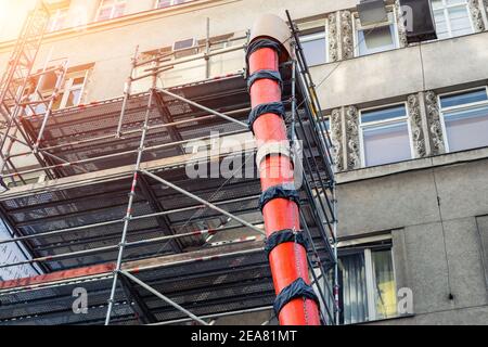 Scaffolding with big red plastic slide chute for rubble debris removal on old historica building facade renewal construction site in city street Stock Photo