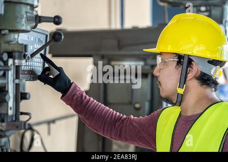 Asian factory engineer in safety suit operating and pressing the professional machinist and lathes for setting the automatic machine in metalworking f Stock Photo