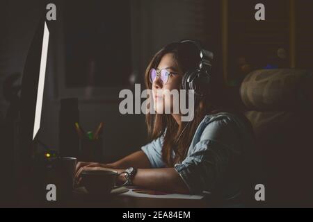 Portrait of Asian Businesswoman sitting and working hard on the table with front of computer desktop in workplace at late with serious action, Work ha Stock Photo