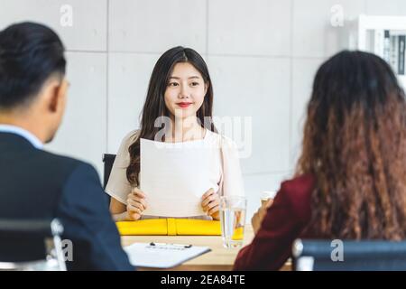 Young Asian woman graduate holding the resume document and preparing to two manager before start to job interview with positive motion in meeting room Stock Photo