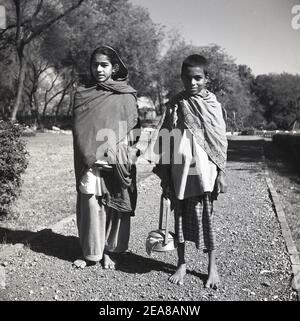 1950s, historical portrait by J Alan Cash of a brother and sister in traditional ethnic dress, wearing silk shawls wrapped around them, standing in barefeet on a gravel path, India. Stock Photo