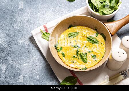 homemade egg omelet with spinach in a frying pan on a gray concrete background Stock Photo