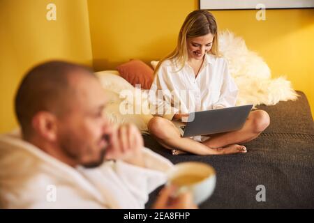 Pleased female working on her laptop next to her spouse Stock Photo