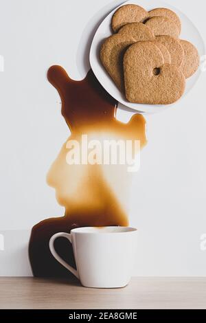 Modern still life of heart shaped gingerbread cookies on a plate and a cup of coffee spilled on the table. Stock Photo