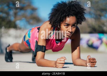 Afro athletic woman doing pushups outdoors. Stock Photo