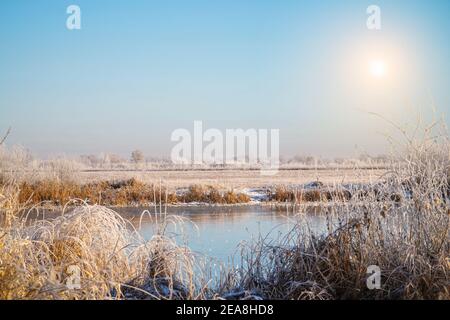 Sun over the winter small pond. Meadows, bushes and trees covered with frost. Fabulous Winter landscape Stock Photo