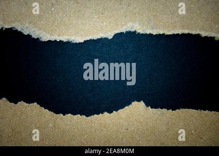 Ripped brown paper on black background, space for copy. Stock Photo