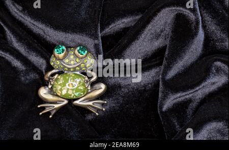 Brooch frog with big green eyes on a black velvet background. Stock Photo