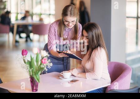Attractive young waitress using a tablet computer to take an order from a customer in a coffee shop Stock Photo