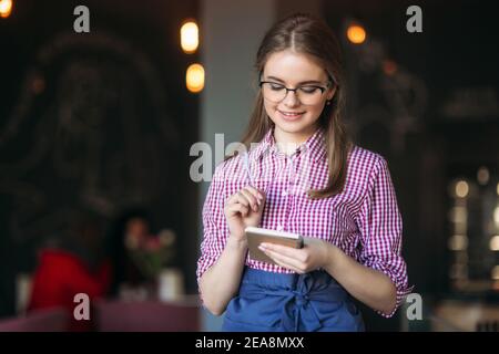 Portrait of a beautiful friendly waitress in glasses with notepapers and pen ready to take your order Stock Photo