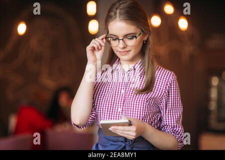 Portrait of a beautiful friendly waitress in glasses with notepapers and pen ready to take your order Stock Photo