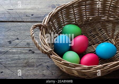 Colored easter eggs in a wicker basket on a wooden surface, space Stock Photo