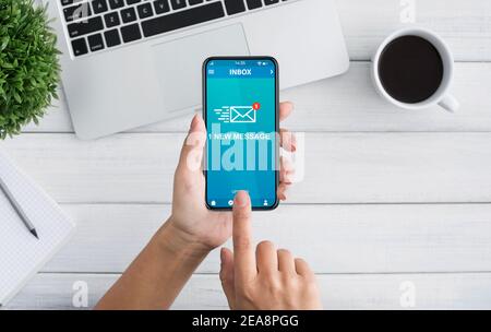 Woman Holding Smartphone With New E-Mail Message Notification At Workplace Stock Photo