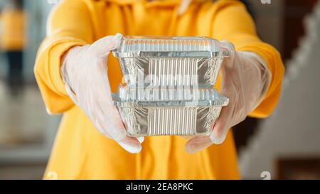 Metal takeaway food container to go. Takeaway Food delivery. Woman in gloves work with takeaway orders. Waiter giving takeout meal while city covid 19 Stock Photo