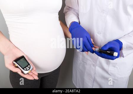 Female Obstetrician doctor measuring blood sugar of the pregnant woman on colorful background. Concept of gestational diabetes in a pregnant girl. Stock Photo