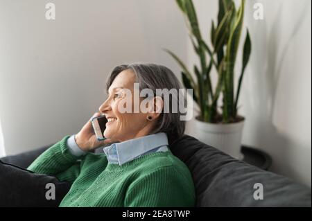 Portait of a relaxed smiling senior mature lady wearing casual wear and calling to her friend, checking up on her family, happy grandmother staying at Stock Photo