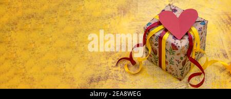 gift wrap on yellow background, gray gift with red and yellow ribbons, Valentine's day February 14 Stock Photo