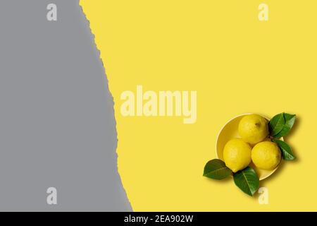Lemons and green leaves yellow bowl on yellow background with cope space Stock Photo