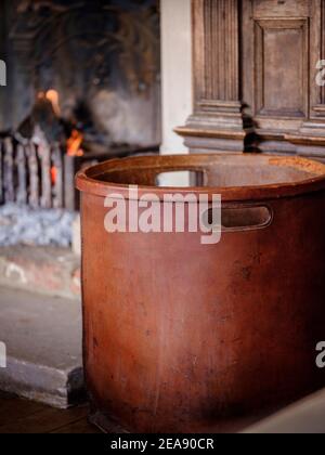 A leather log basket beside a warm open fire with glowing embers in a wood-panelled country house. Stock Photo
