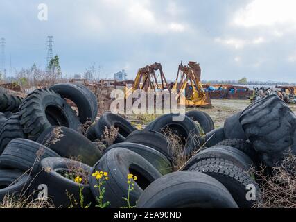 Industrial graveyard with discarded large tires and heavy equipment attachments along the river Stock Photo